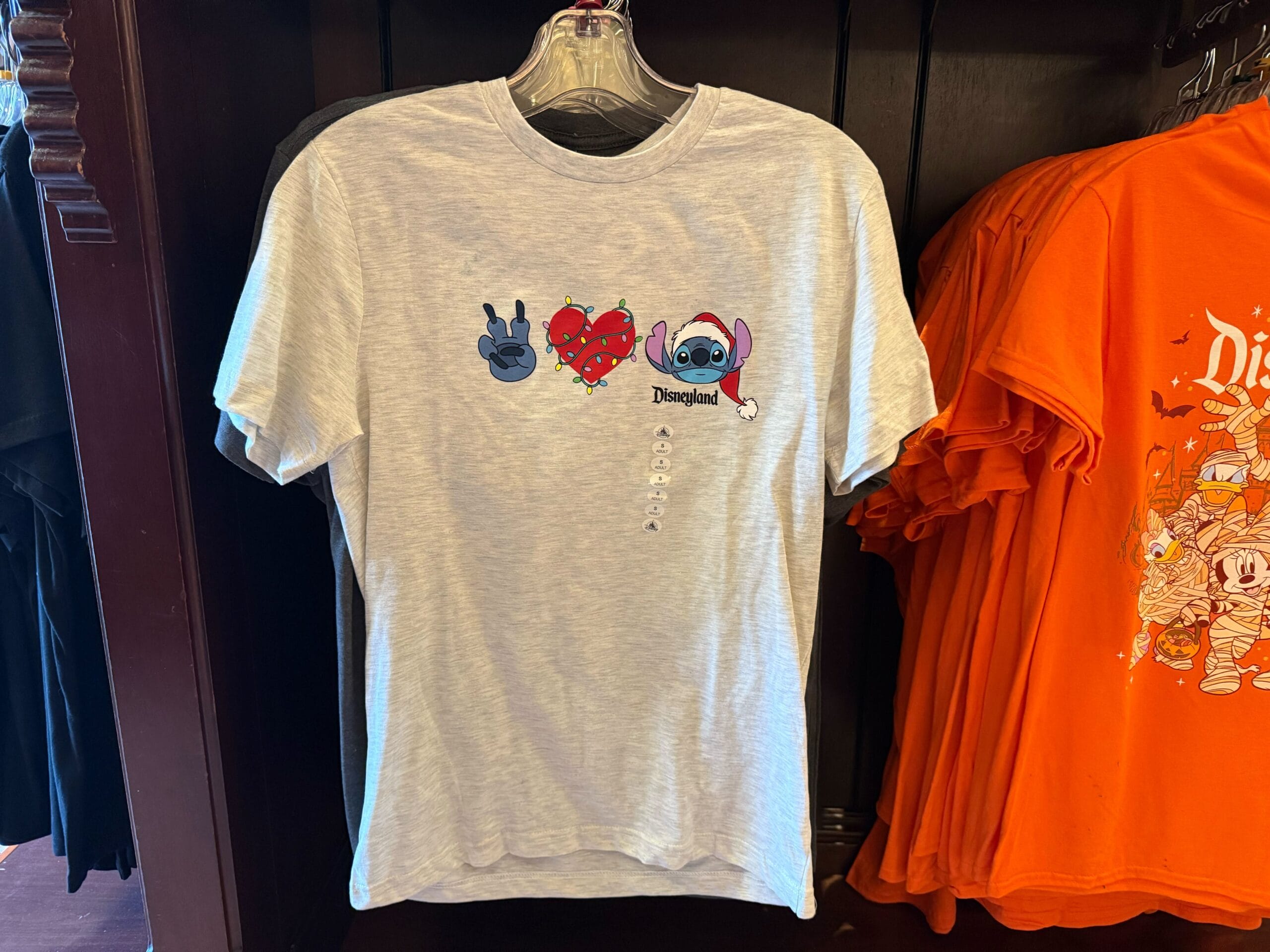 Light gray Disneyland t-shirt with Stitch hand signs, red heart, and "Disneyland"—perfect Christmas merchandise on a rack.
