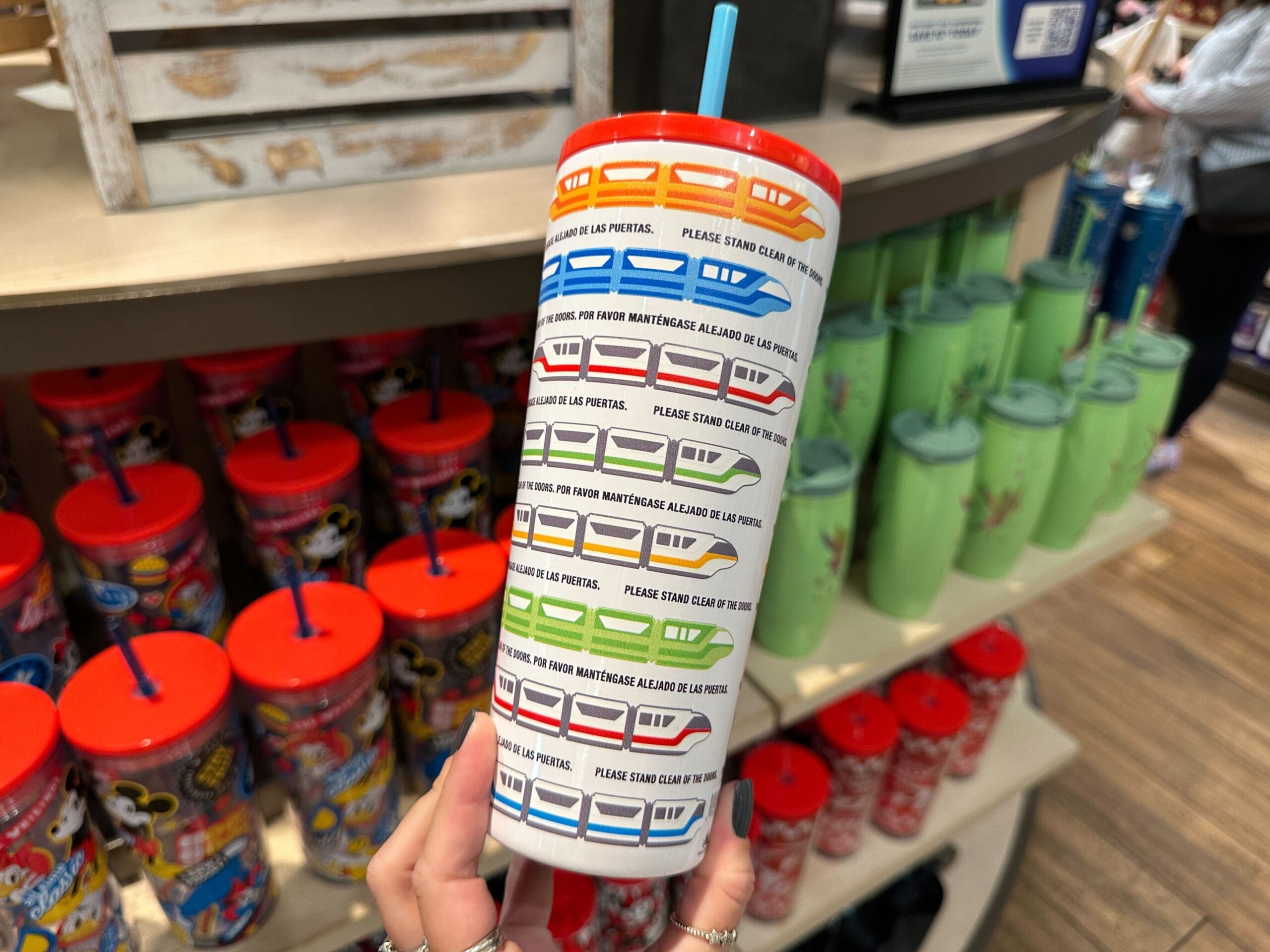 Hand holding a colorful Monorail Tumbler at World of Disney in Disney Springs, surrounded by other vibrant cups.