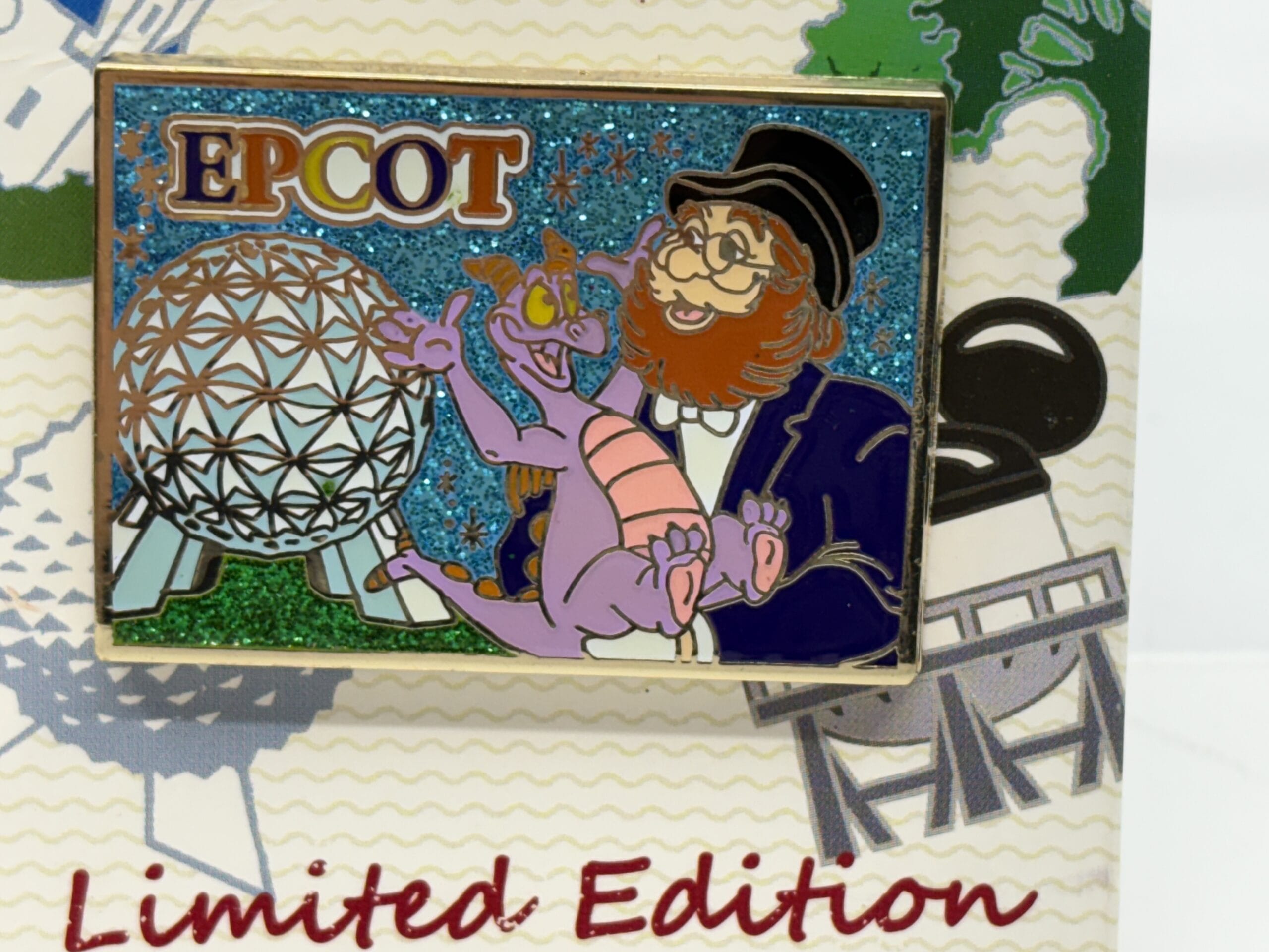 A colorful pin from the wdwnt summer auction shows EPCOT’s Spaceship Earth, Figment, and a man with glasses on glittery background.