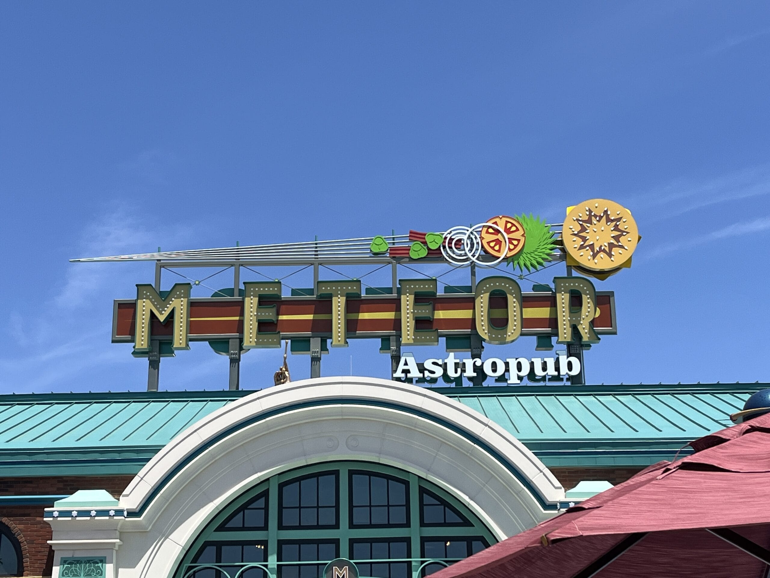 Meteor Astropub sign with a meteor-shaped drink garnish, set against a clear blue sky.