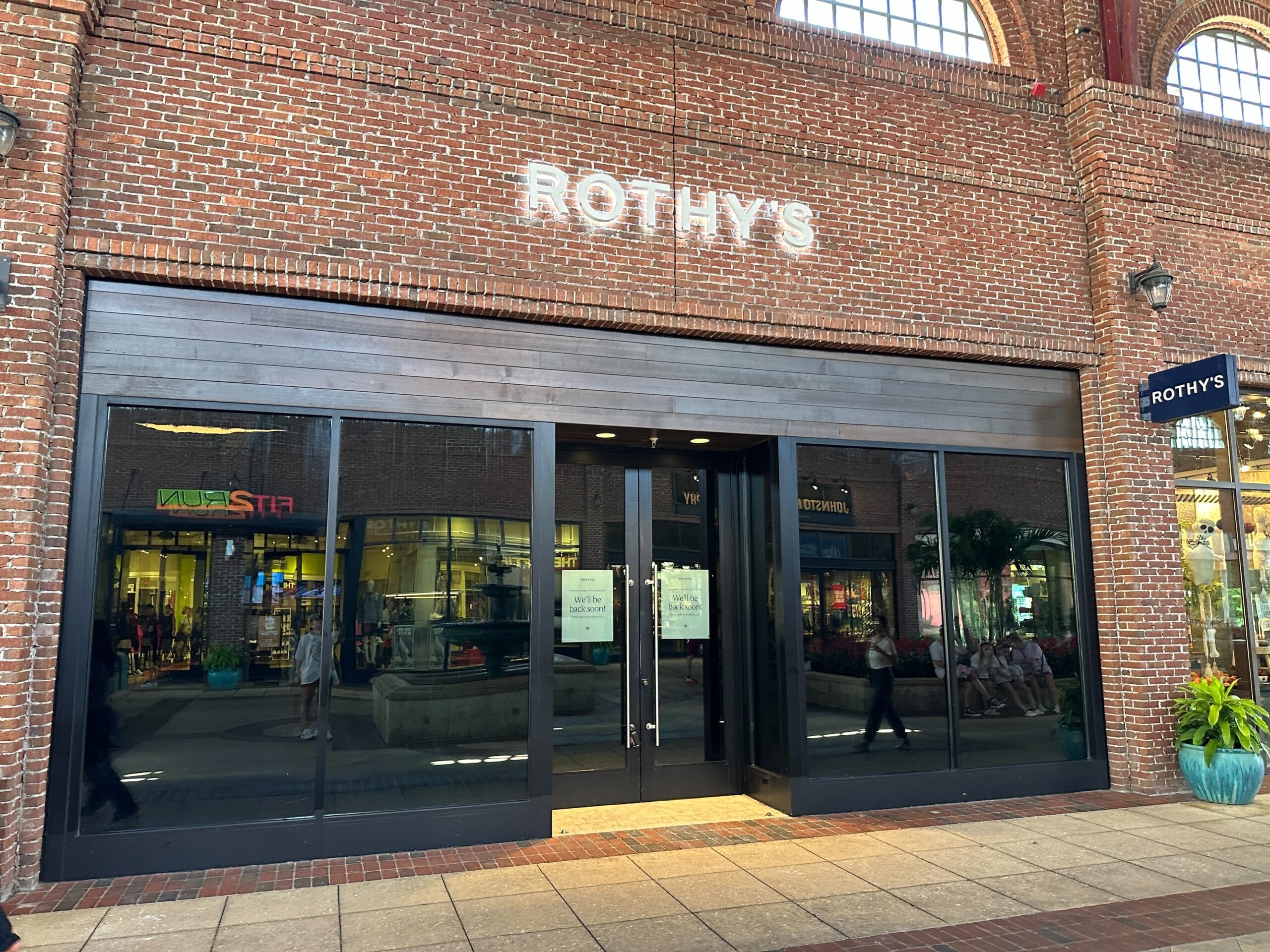 Storefront of Rothy’s with large glass doors, brick exterior, near Disney World and shops visible through the windows.