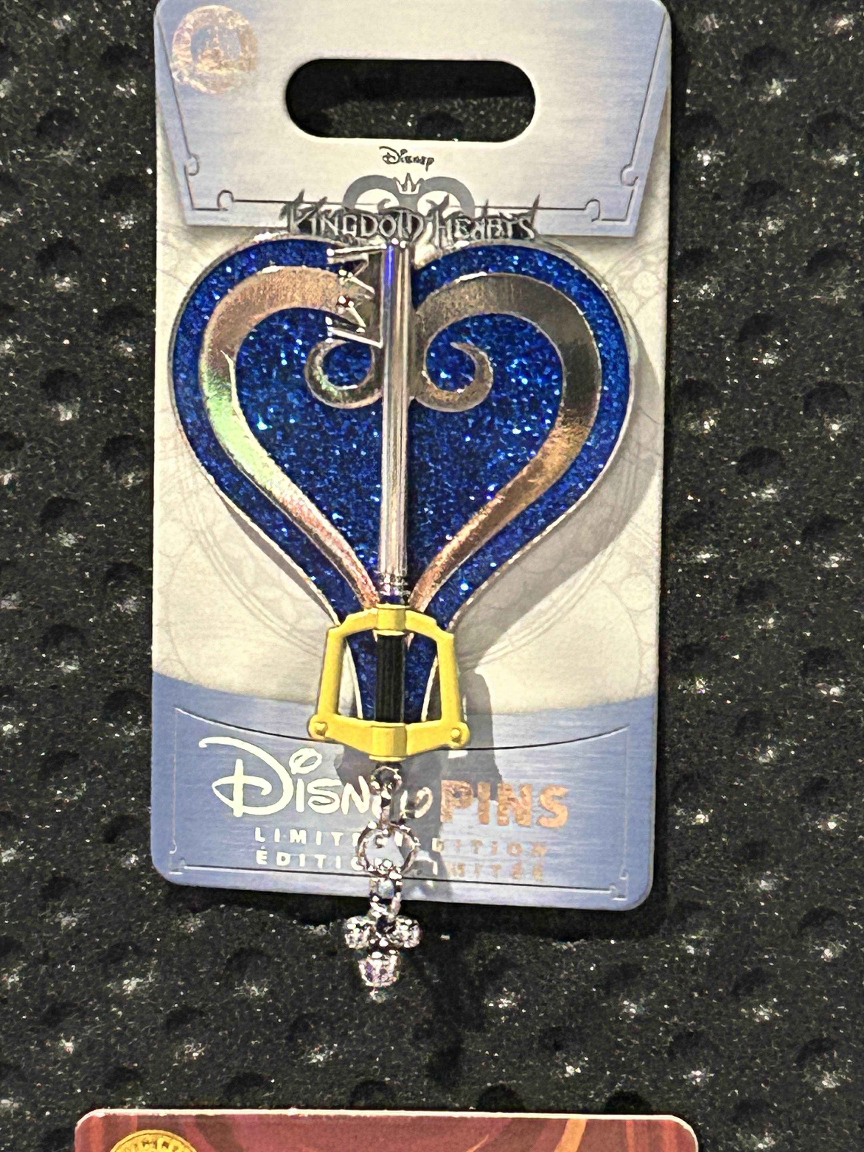 A blue glittery Kingdom Hearts Pin of the Month on a Disney card, displayed against a textured black background.