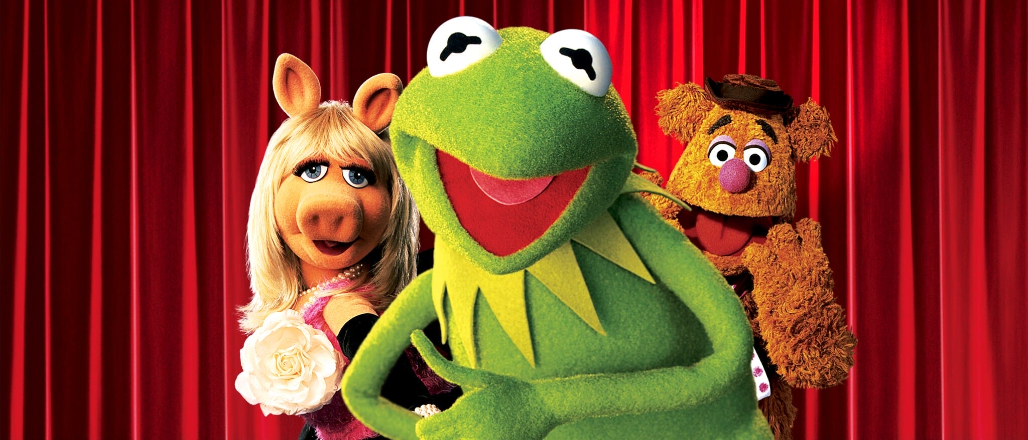 Kermit the Frog, Miss Piggy, and Fozzie Bear pose together for a Daily Recap in front of a red stage curtain.