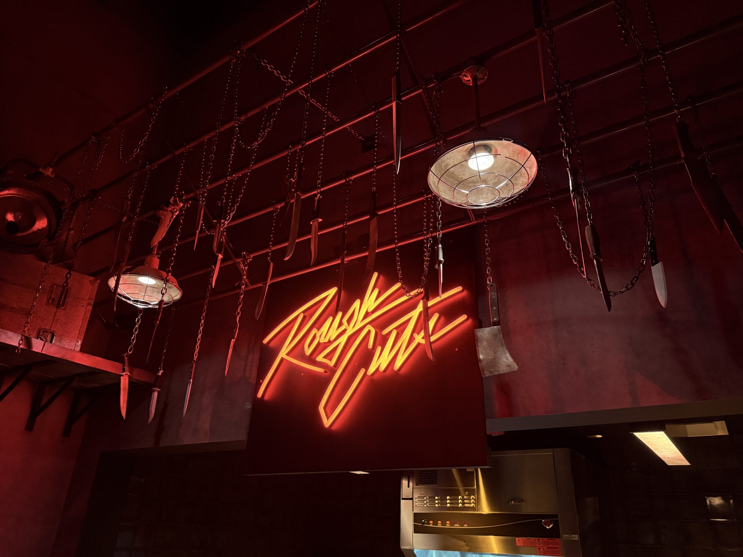 A red neon "Rough Cuts" sign glows under chains and knives hanging from the ceiling in Universal Horror Unleashed - Las Vegas.
