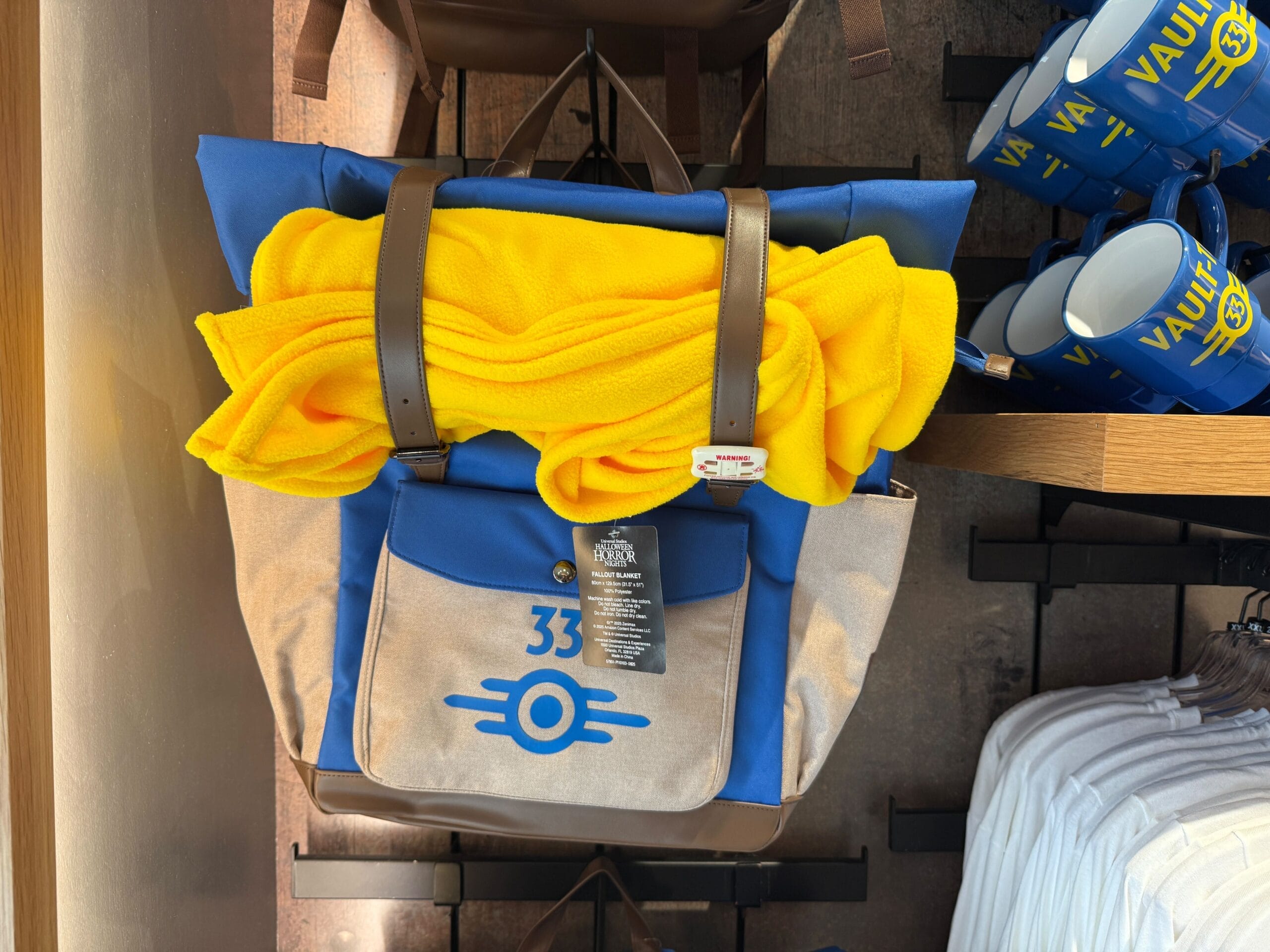 A blue and tan Vault 33 backpack with a yellow blanket hangs in a store at Universal Studios Florida.